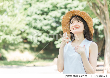 Smiling Asian woman spraying sunscreen and insect repellent on her neck Smiling Asian woman spraying sunscreen and insect repellent on her neck 100938671