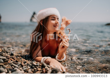 Woman travel sea. Happy tourist enjoy taking picture on the beach for memories. Woman traveler in Santa hat looks at camera on the sea bay, sharing travel adventure journey Woman travel sea. Happy tourist enjoy taking picture on the beach for memories. Woman traveler in Santa hat looks at camera on the sea bay, sharing travel adventure journey 100943313