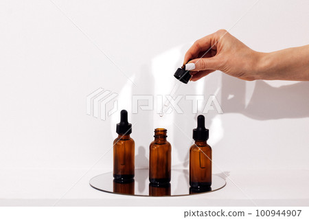Serum or essence glass three bottles on the mirror and womans hand with a pipette above them. Serum or essence glass three bottles on the mirror and womans hand with a pipette above them. 100944907