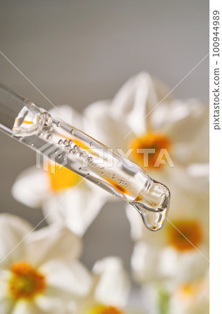 An eyedropper with a cosmetic product on the background of daffodils. 100944989