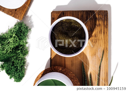 Plastic jar with green collagen eye patches on cork stage. Aloe plant, wooden shap and collagen 100945159