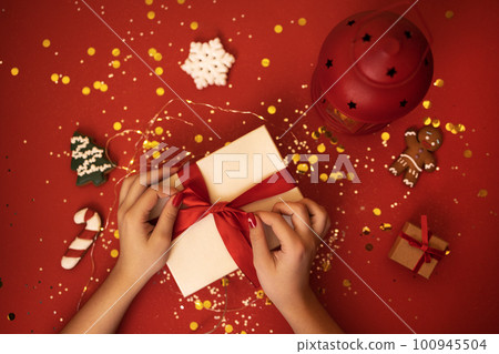 Female hands with red manicure decorate gift box with red ribbon and bow. 100945504