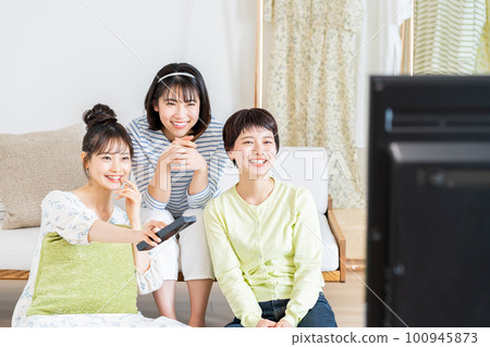 Young woman watching TV with her friends in the living room 100945873