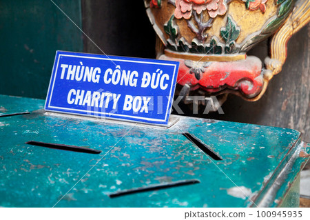 Green donation box with a sign in Vietnamese and English in a temple. A charity box with multiple slits for offering money to support a cause Green donation box with a sign in Vietnamese and English in a temple. A charity box with multiple slits for offering money to support a cause 100945935