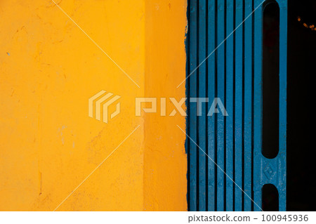Yellow and blue abstract background divided in two halves vertically. Brightly colored wall and folding gate of a Vietnamese house Yellow and blue abstract background divided in two halves vertically. Brightly colored wall and folding gate of a Vietnamese house 100945936