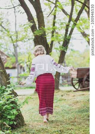 beautiful peasant woman in embroidered clothes walks around the yard 100946530
