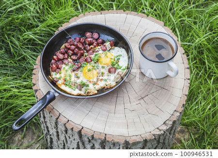 scrambled eggs with sausage and coffee on a stump in the forest 100946531