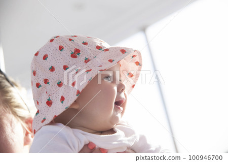 newborn girl in hat looks at the sunset and smiles toothlessly 100946700
