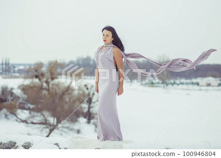 Attractive woman in evening dress on a hill in winter 100946804