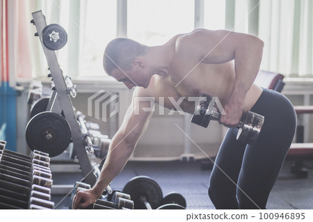 Athlete trains back muscles by lifting a dumbbell 100946895