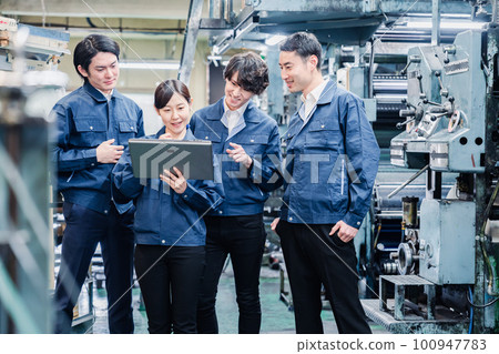 Factory staff having a meeting while looking at a tablet terminal 100947783