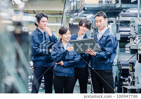 Factory staff having a meeting while looking at a tablet terminal 100947786