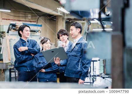 Factory staff having a meeting while looking at a tablet terminal 100947790