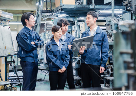 Factory staff having a meeting while looking at a tablet terminal 100947796