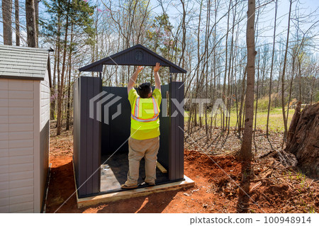 Worker is putting together plastic vinyl storage shed for backyard nearby 100948914