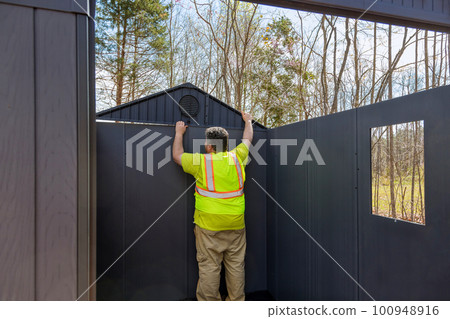 There is worker assembling plastic vinyl storage shed for backyard near house 100948916
