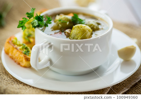 Hot cooked soup with Brussels sprouts, vegetables and croutons, in a plate. 100949360