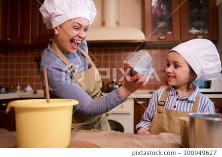 Happy cheerful family, loving mother and cute little daughter have fun together, enjoying festive atmosphere in kitchen while cooking Easter cake, pastries and panettone. People. Lifestyles. Leisures 100949627