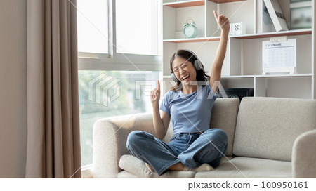 Young Asian woman happily listening to music through headphones, Woman was enjoying listening to her favorite music and rocking to the beat of the music, Stress relief, Happiness in life. 100950161