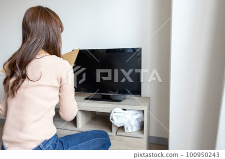 Rear view of a young woman turning on the TV in her new studio apartment 100950243