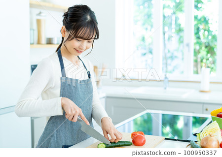 Young woman in apron cooking in the kitchen 100950337