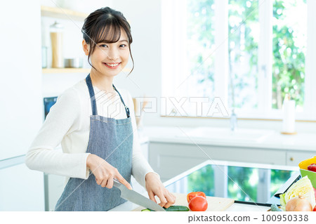 Young woman in apron cooking in the kitchen 100950338