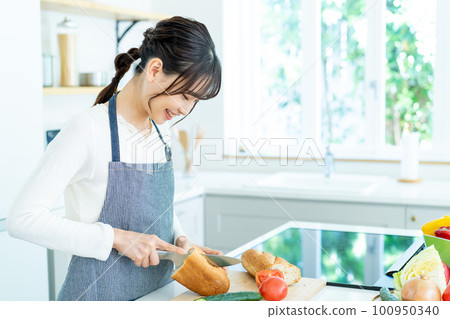 Young woman in apron cooking in the kitchen 100950340