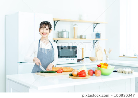 Young woman in apron cooking in the kitchen 100950347