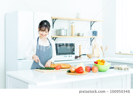Young woman in apron cooking in the kitchen 100950348
