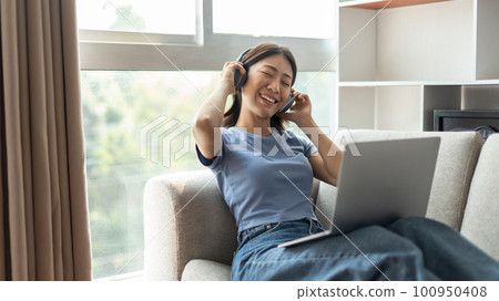 Young Asian woman happily listening to music through headphones, Woman was enjoying listening to her favorite music and rocking to the beat of the music, Stress relief, Happiness in life. Young Asian woman happily listening to music through headphones, Woman was enjoying listening to her favorite music and rocking to the beat of the music, Stress relief, Happiness in life. 100950408