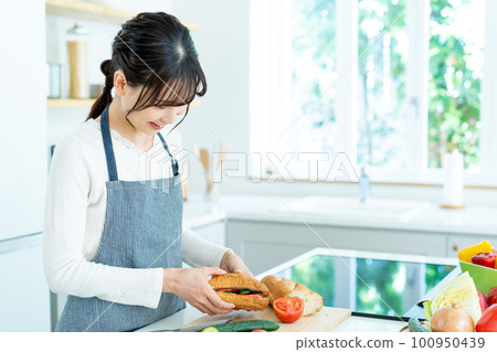 Young woman in apron cooking in the kitchen 100950439