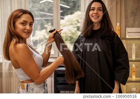 Pretty brunette young woman looks into a huge mirror when her luxurious long hair is cut off 100950516