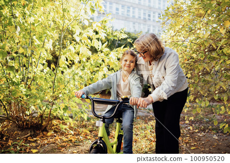 Young grandmother teaches her cute little granddaughter to ride a bicycle Young grandmother teaches her cute little granddaughter to ride a bicycle 100950520