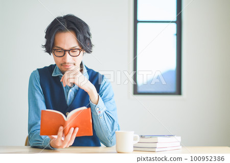 Young man reading a book in his study at home Young man reading a book in his study at home 100952386