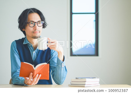 年輕人在家裡的書房裡邊喝咖啡邊看書 年輕人在家裡的書房裡邊喝咖啡邊看書 100952387