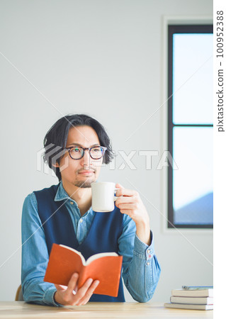 年輕人在家裡的書房裡邊喝咖啡邊看書 年輕人在家裡的書房裡邊喝咖啡邊看書 100952388