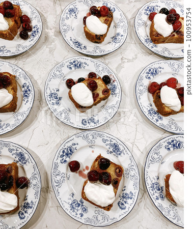 Pattern of plates with a sweet dessert on them. Appetizing slices of pie with cherries, berries and cream on beautiful plates with blue painting and flowers. 100953754