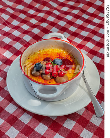 Sweet baked dessert in a deep porcelain white plate with handles. The dish is decorated with currants and blueberries. Sweet baked dessert in a deep porcelain white plate with handles. The dish is decorated with currants and blueberries. 100953755