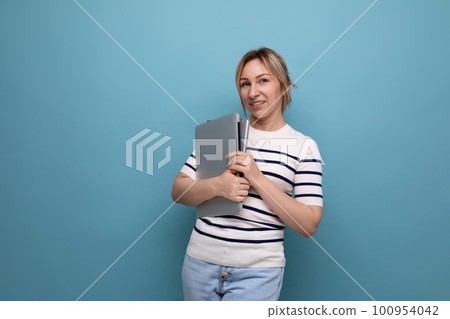 close-up of a confident blonde woman in a striped sweater holding a laptop in her hands on a blue close-up of a confident blonde woman in a striped sweater holding a laptop in her hands on a blue 100954042