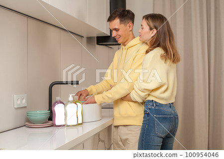 Lovely couple hugging and washing the dishes using dishwashing liquid with blank label Lovely couple hugging and washing the dishes using dishwashing liquid with blank label 100954046