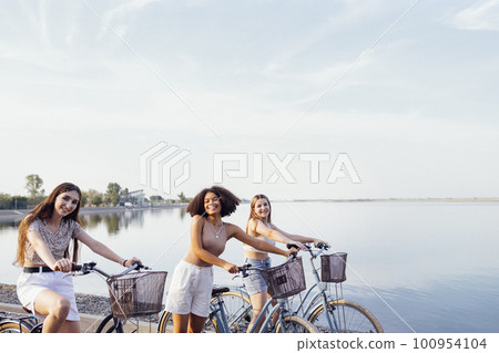 Teenagers of different nationalities and appearance on bicycles ride along a city street 100954104
