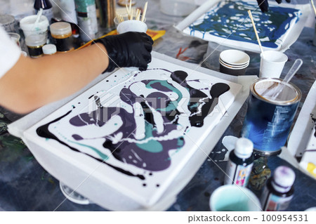 Master class on an Acrylic Fluid Pouring. Young women paint with liquid acrylic in an art workshop Master class on an Acrylic Fluid Pouring. Young women paint with liquid acrylic in an art workshop 100954531