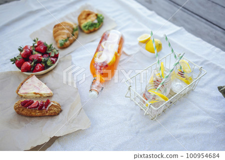 Bottle of strawberry and lemon smoothie, soda glasses with straws, herb croissants, sweet cakes and fresh strawberries 100954684