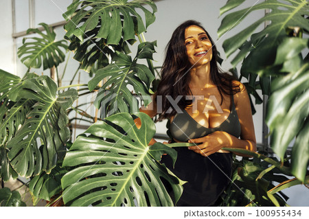 beautiful brunette female expecting a child stands in monstera leaves 100955434