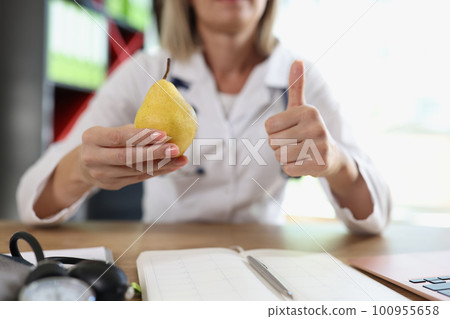 Doctor holds ripe pear in hand making thumb up gesture Doctor holds ripe pear in hand making thumb up gesture 100955658