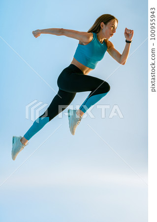 Determined sporty woman running in Mid-Air exercising during cardio workout over studio background 100955943