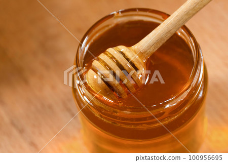 Wooden ladle with honey and a glass jar, on a wooden table close-up. Organic beekeeping products Wooden ladle with honey and a glass jar, on a wooden table close-up. Organic beekeeping products 100956695