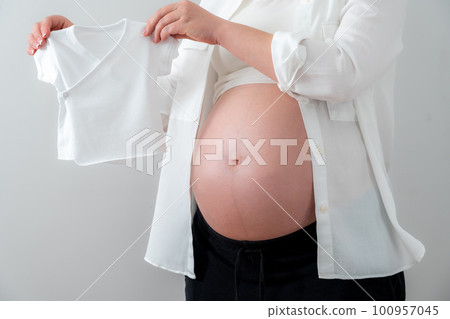 Pregnant woman holding tiny little baby clothes, concept of expecting baby 100957045