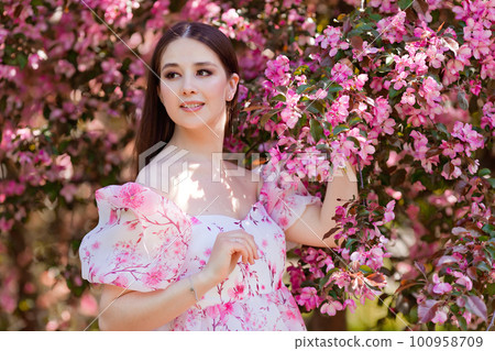 A smiling girl in a pink dress standing near pink blooming trees 100958709