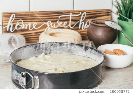 Baking dish with raw apple pie dough stands on kitchen counter next to ingredients and wooden sign Home sweet home 100958771
